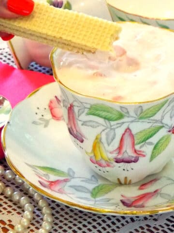 A tea cup with filled with pink pudding with cookie being dipped into it.