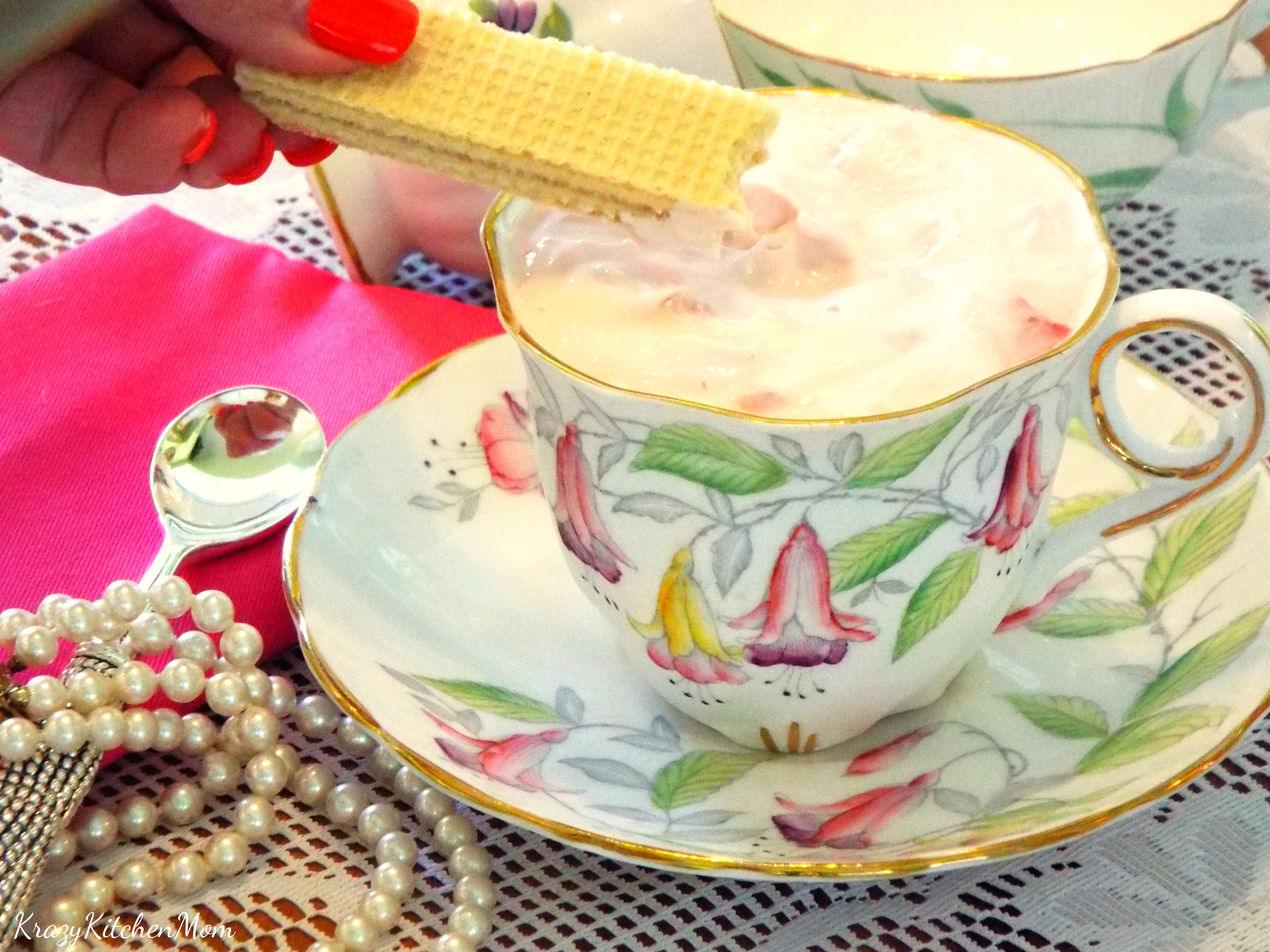 A tea cup with filled with pink pudding with cookie being dipped into it. 