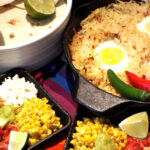 a pan of has browns topped with eggs with corn, lime, tortillas, on side