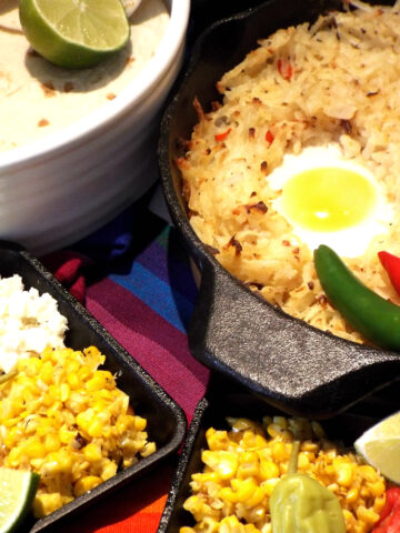 a pan of has browns topped with eggs with corn, lime, tortillas, on side