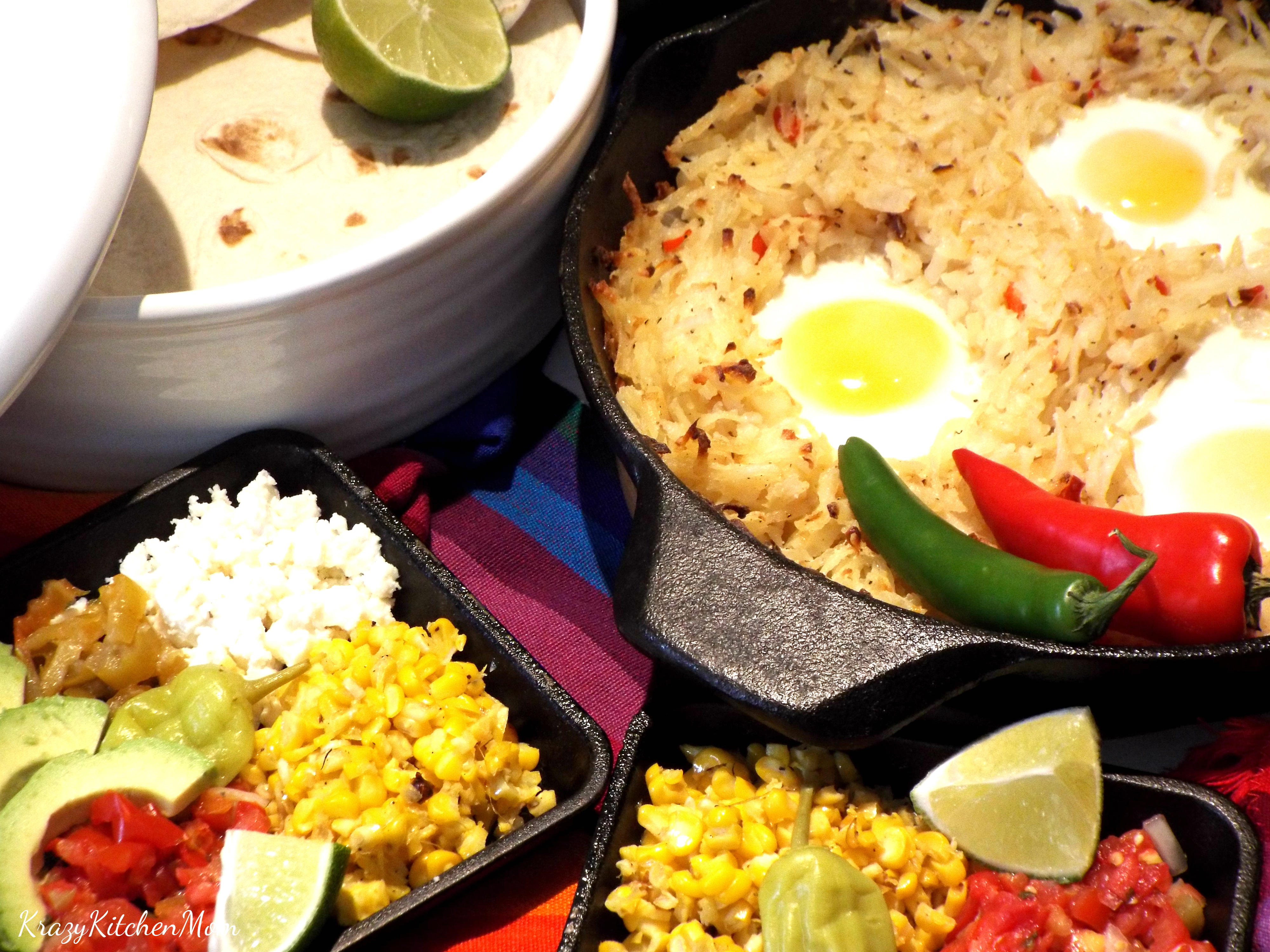 a pan of has browns topped with eggs with corn, lime, tortillas, on side