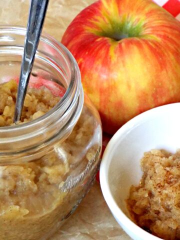 a jar of apples sauce with a spoon and a small dish and apple on the side