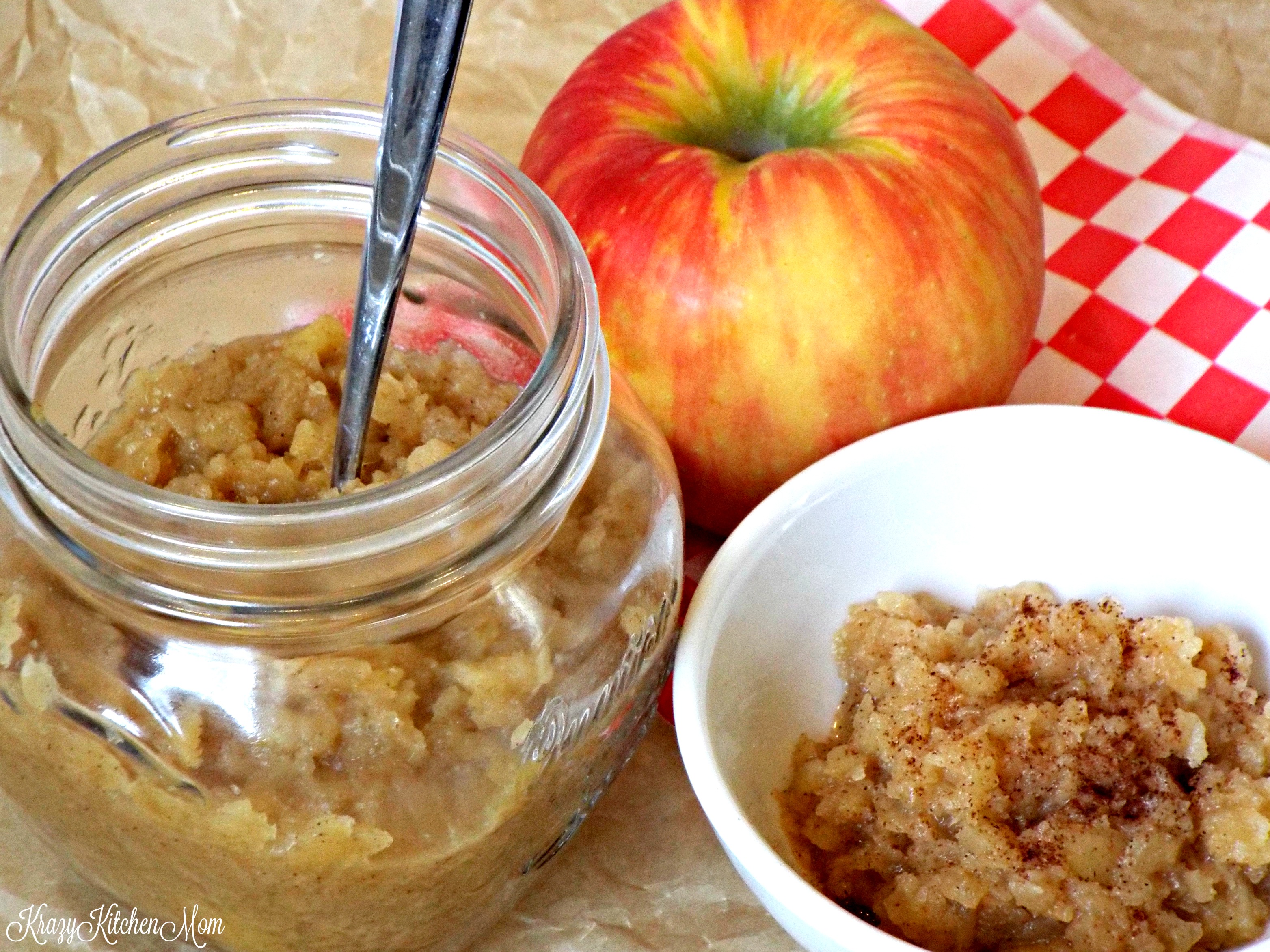 a jar of apples sauce with a spoon and a small dish and apple on the side