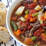 A bowl of beef soup with potatoes, beans, carrots, tomatoes