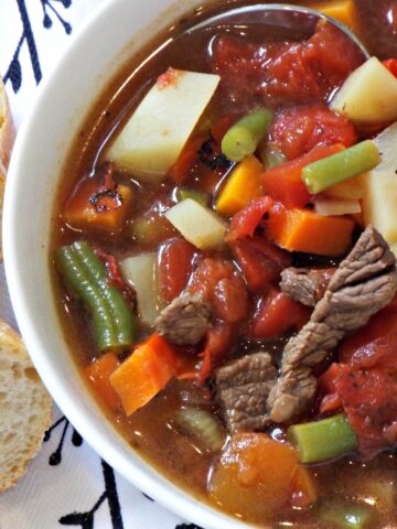 A bowl of beef soup with potatoes, beans, carrots, tomatoes