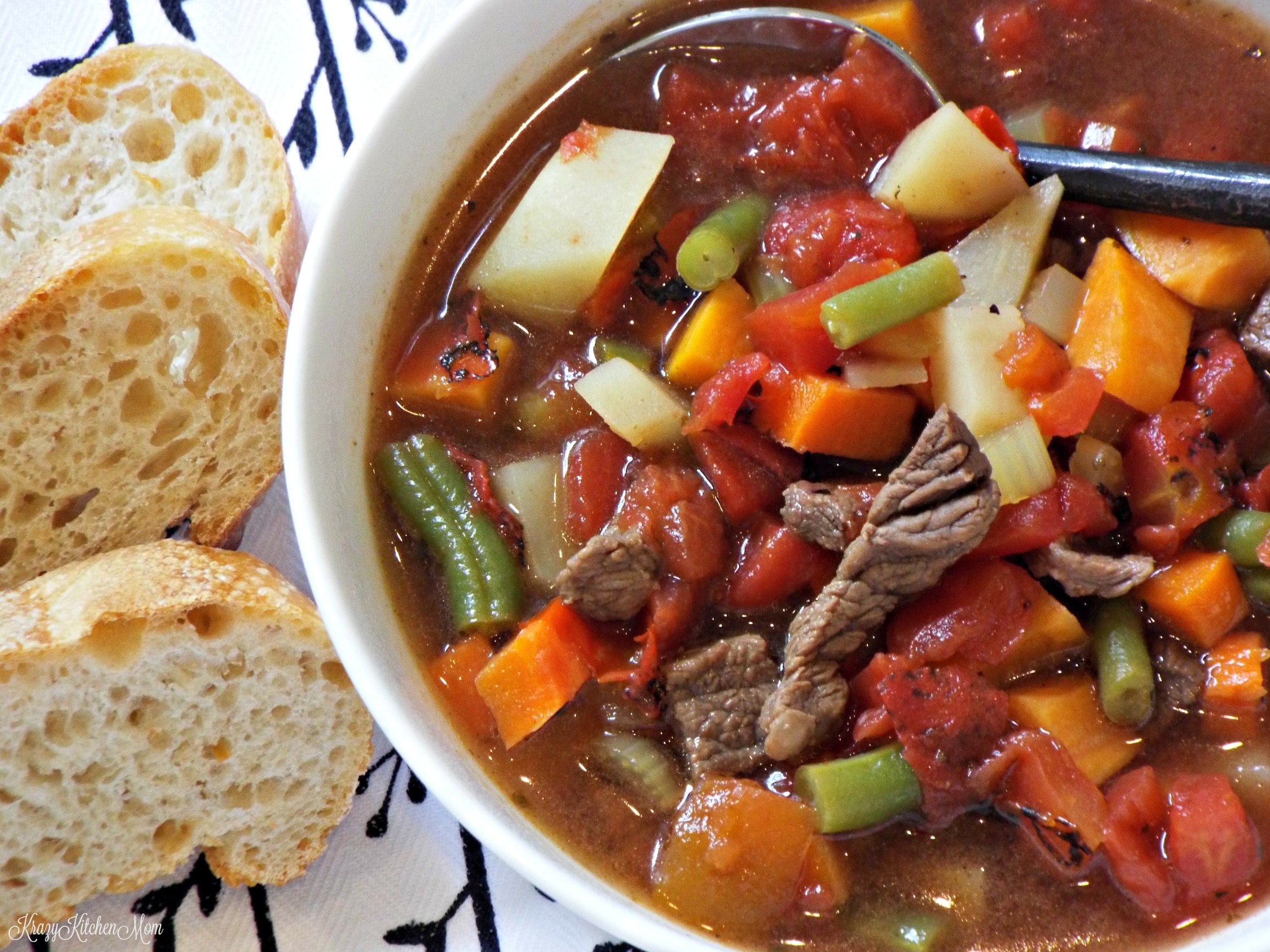 A bowl of beef soup with potatoes, beans, carrots, tomatoes 