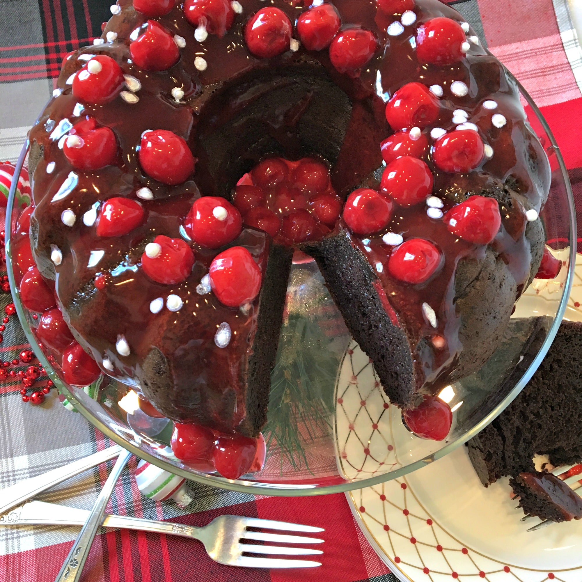 an overhead shot of chocolate cake covered in cherries with forks