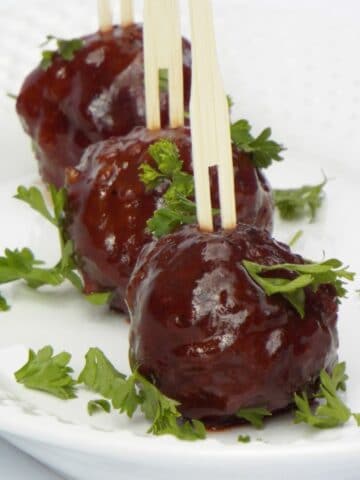 three small meatballs in a row with skewers in them on a white pate with parsley