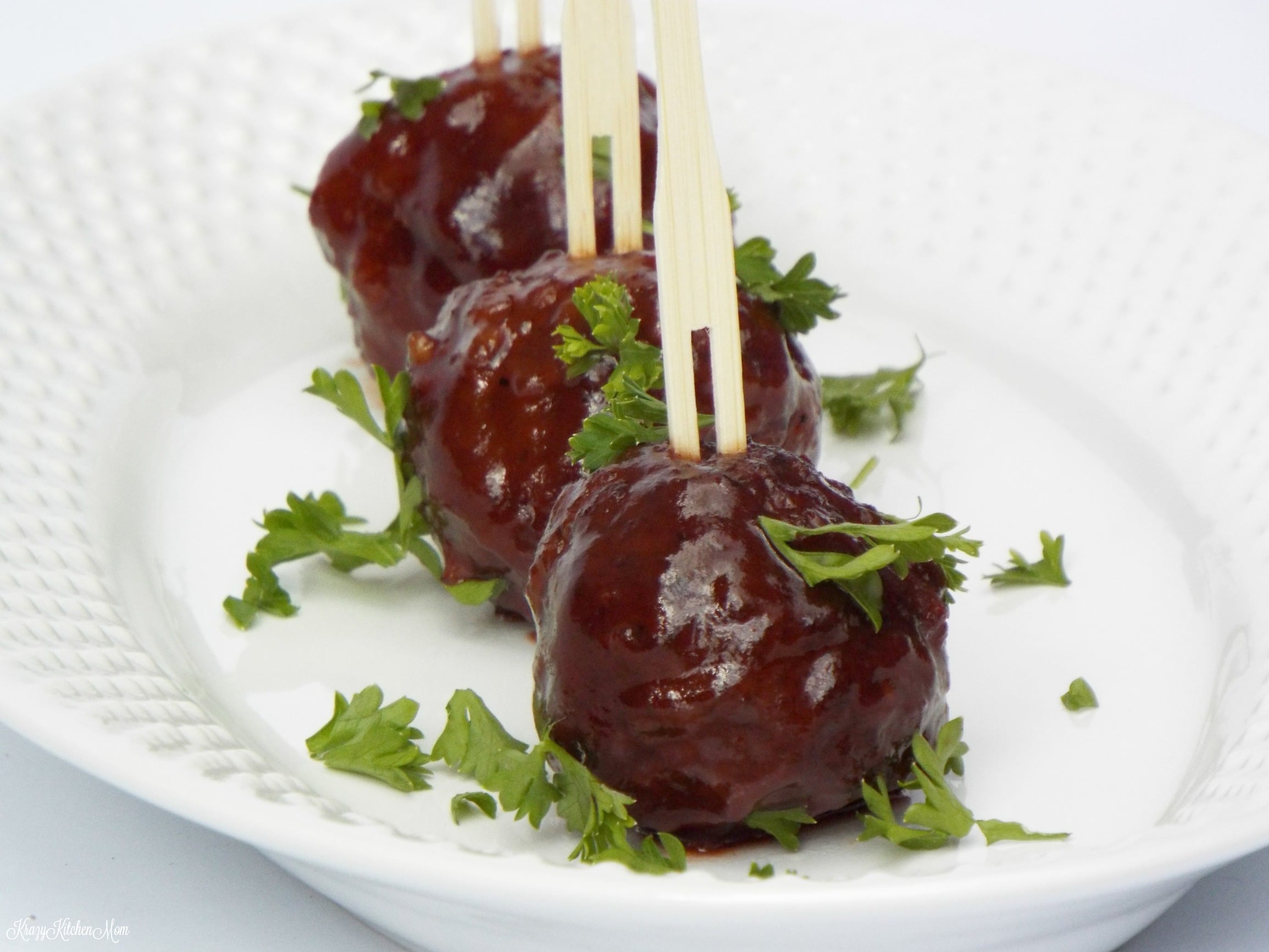 three small meatballs in a row with skewers in them on a white pate with parsley