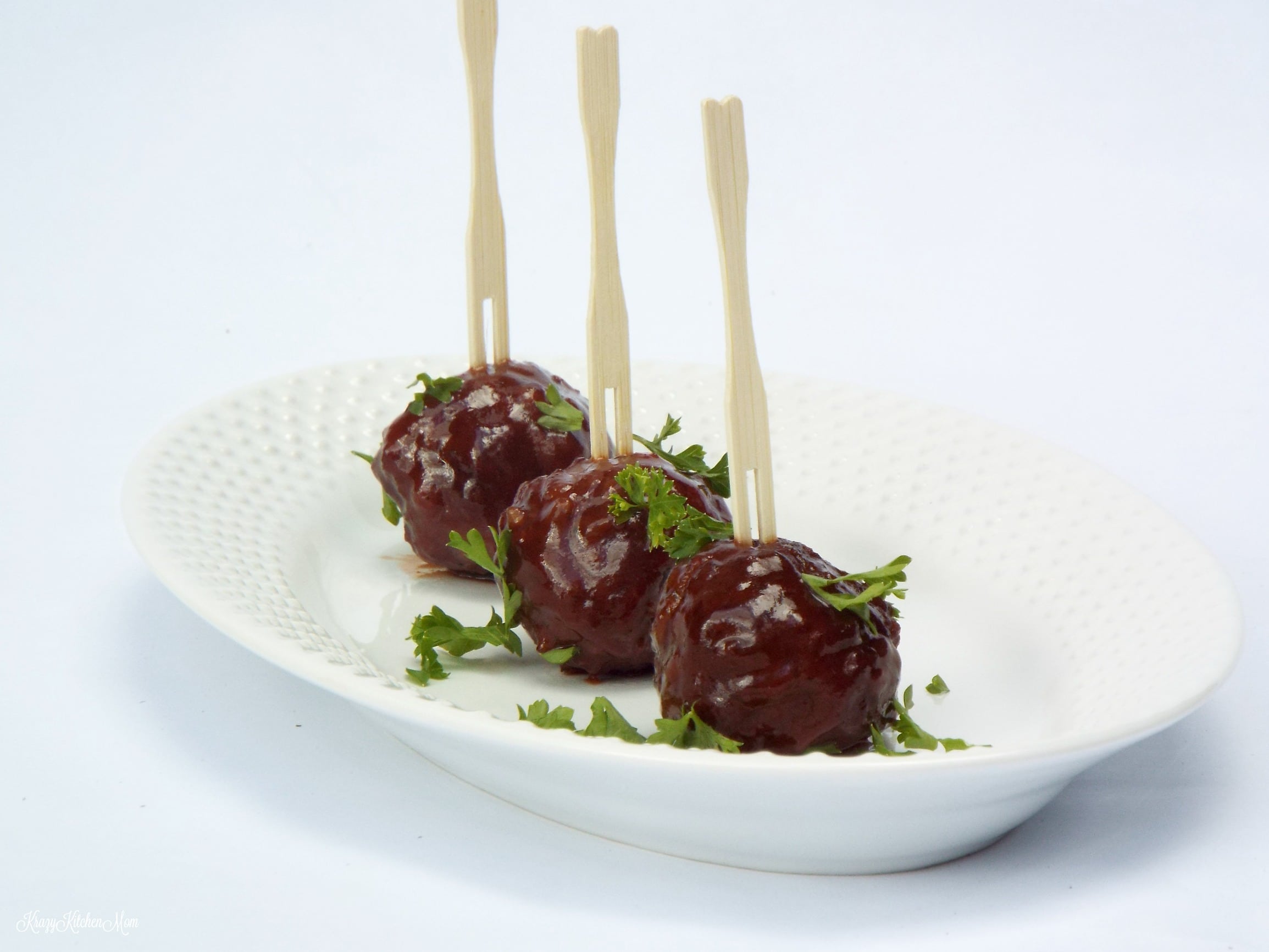 three mini meatballs with skewers on a plate with parsley