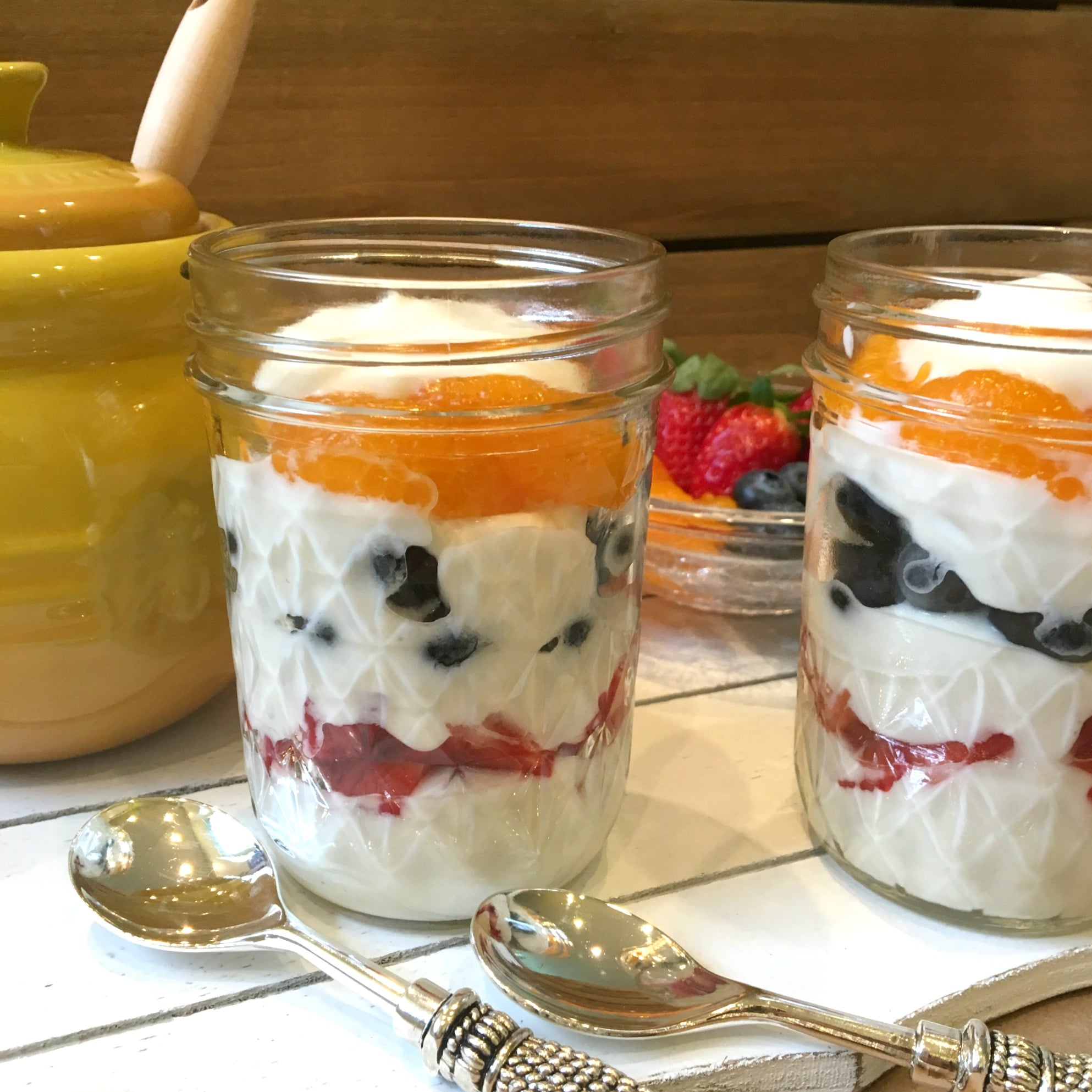 two yogurt parfaits with spoons and yellow jar in background