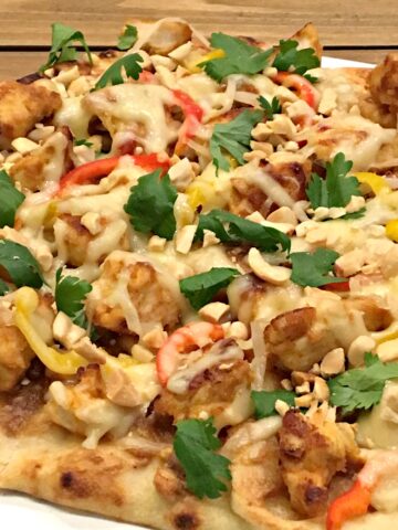 A flatbread topped with chicken, cheese, peanut sauce and cilantro