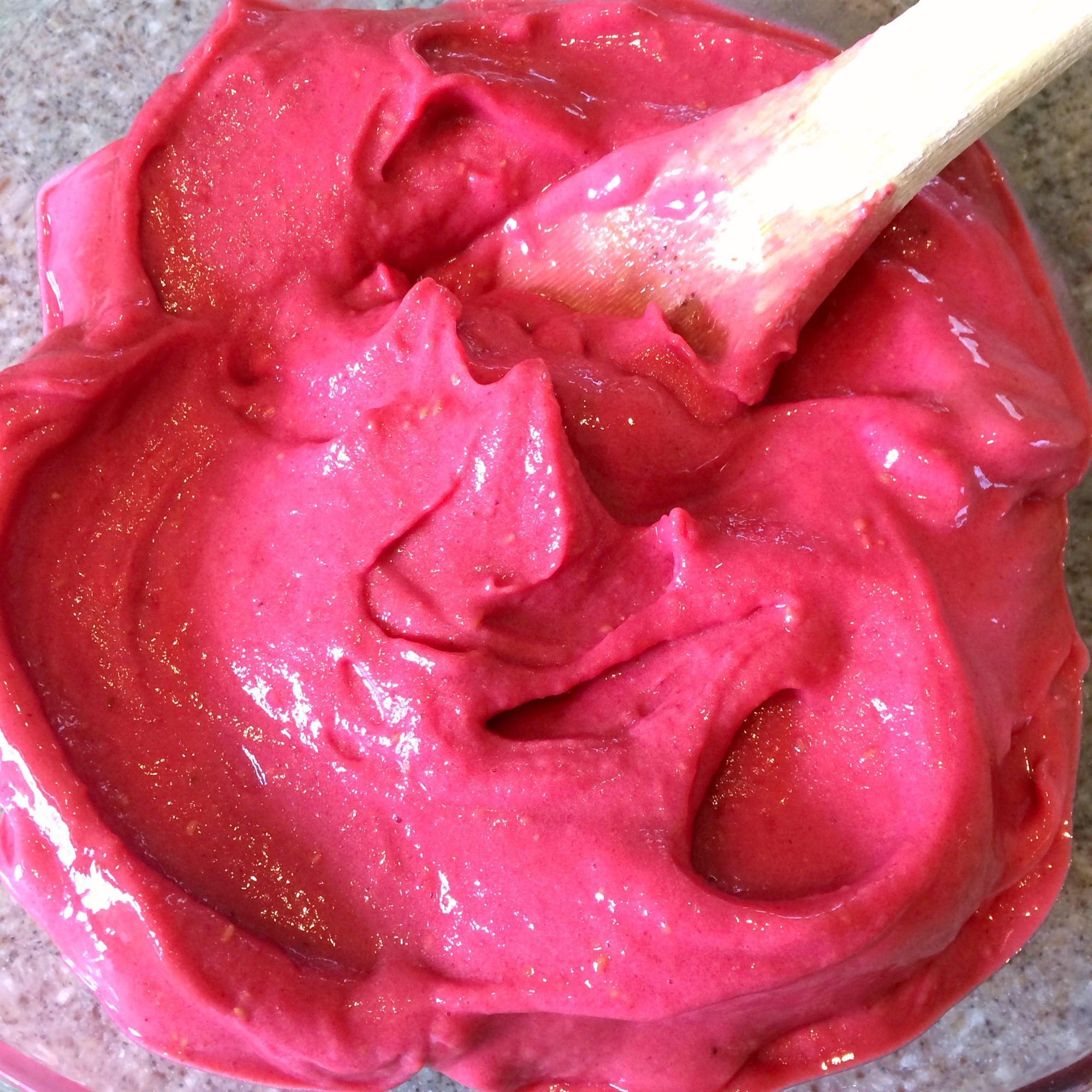 A bowl of hot pink ice cream being stirred with a wooden spoon