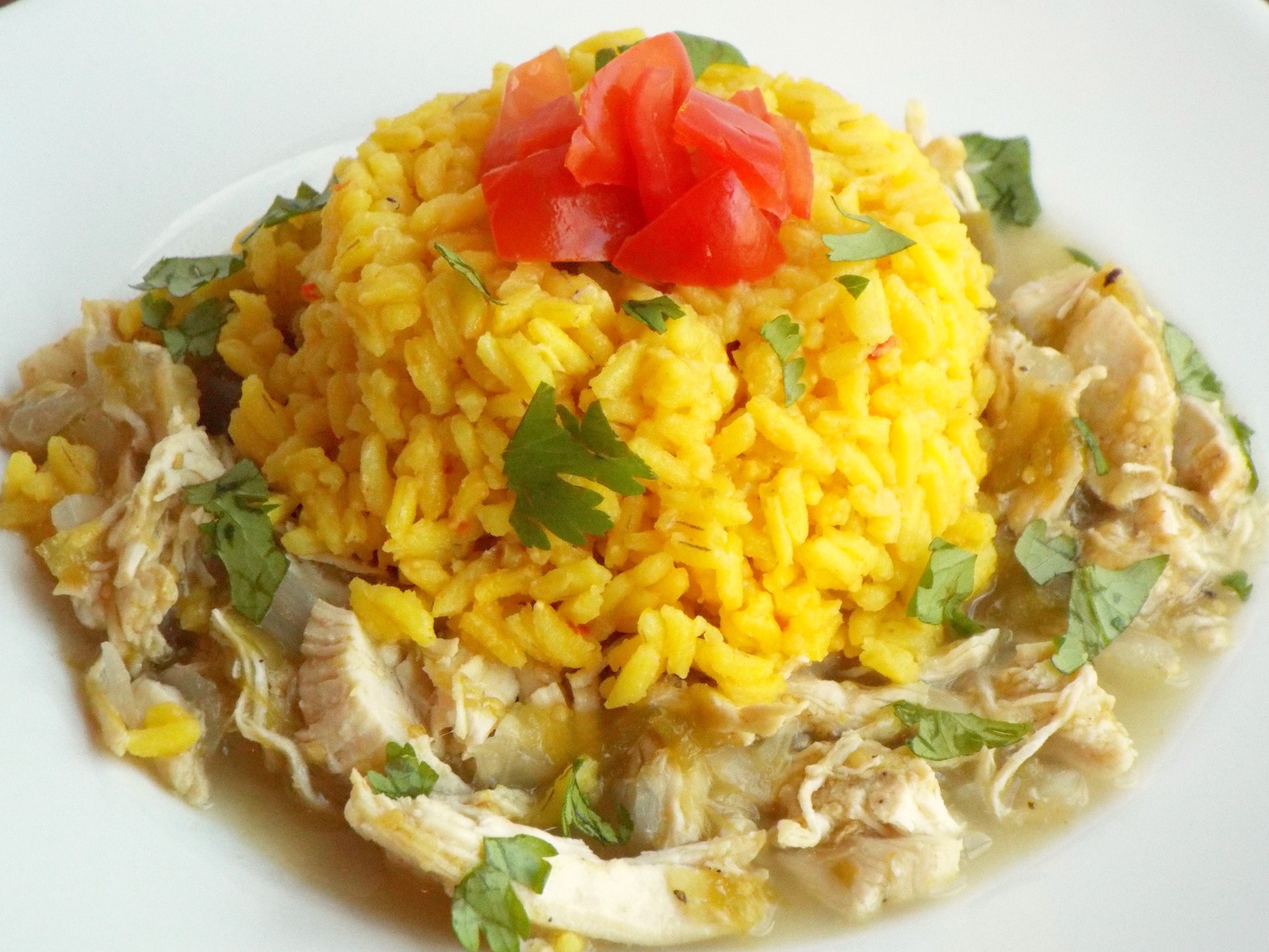 A plate of shredded chicken topped with yellow rice, tomatoes and cilantro