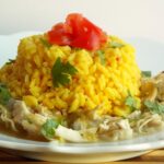 a plate of shredded chicken topped with yellow rice, tomatoes and cilantro