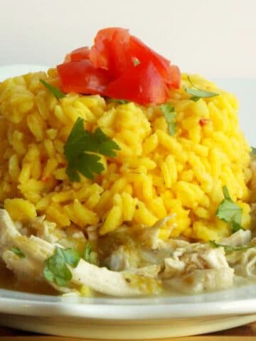 a plate of shredded chicken topped with yellow rice, tomatoes and cilantro