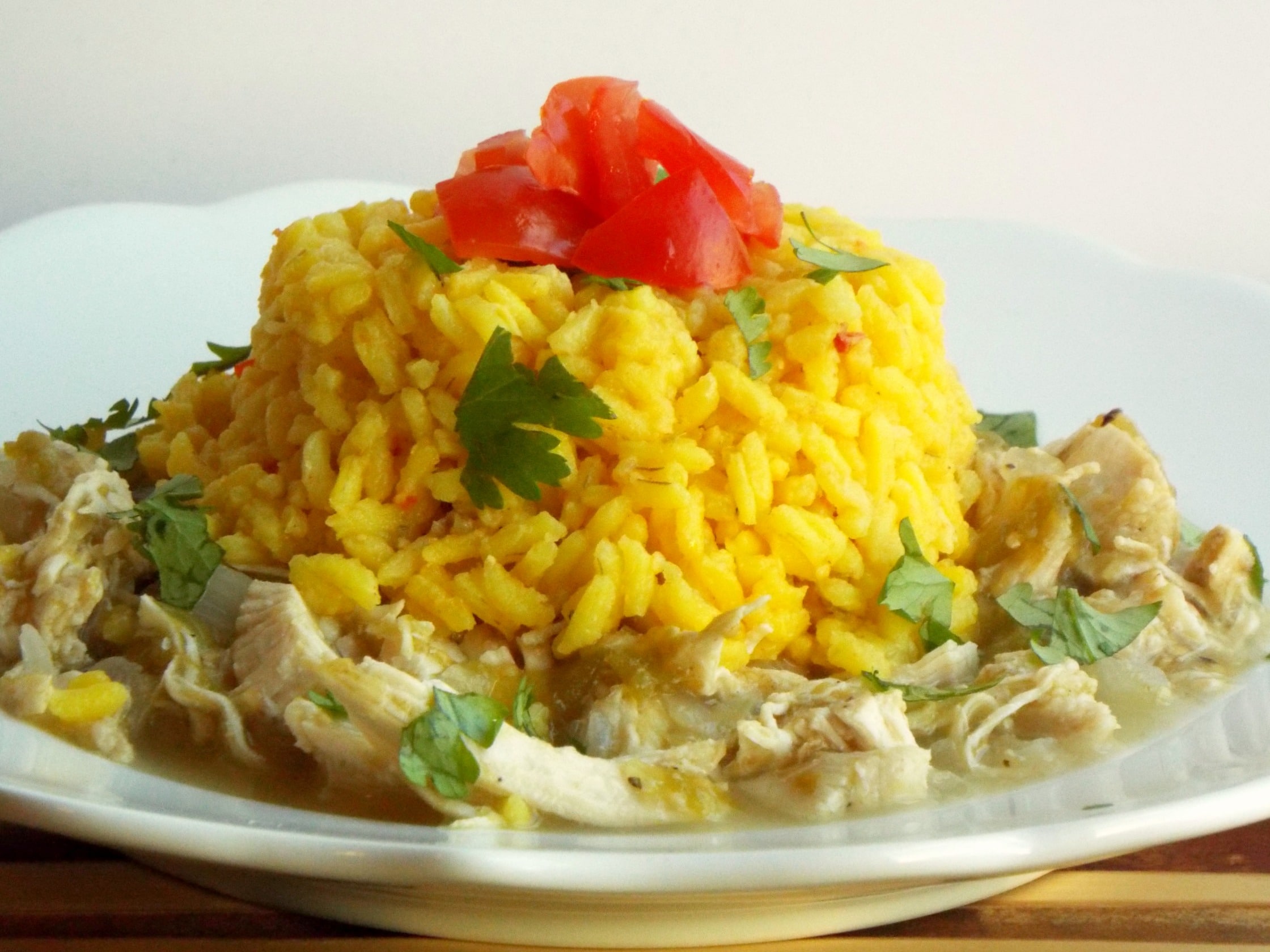 a plate of shredded chicken topped with yellow rice, tomatoes and cilantro