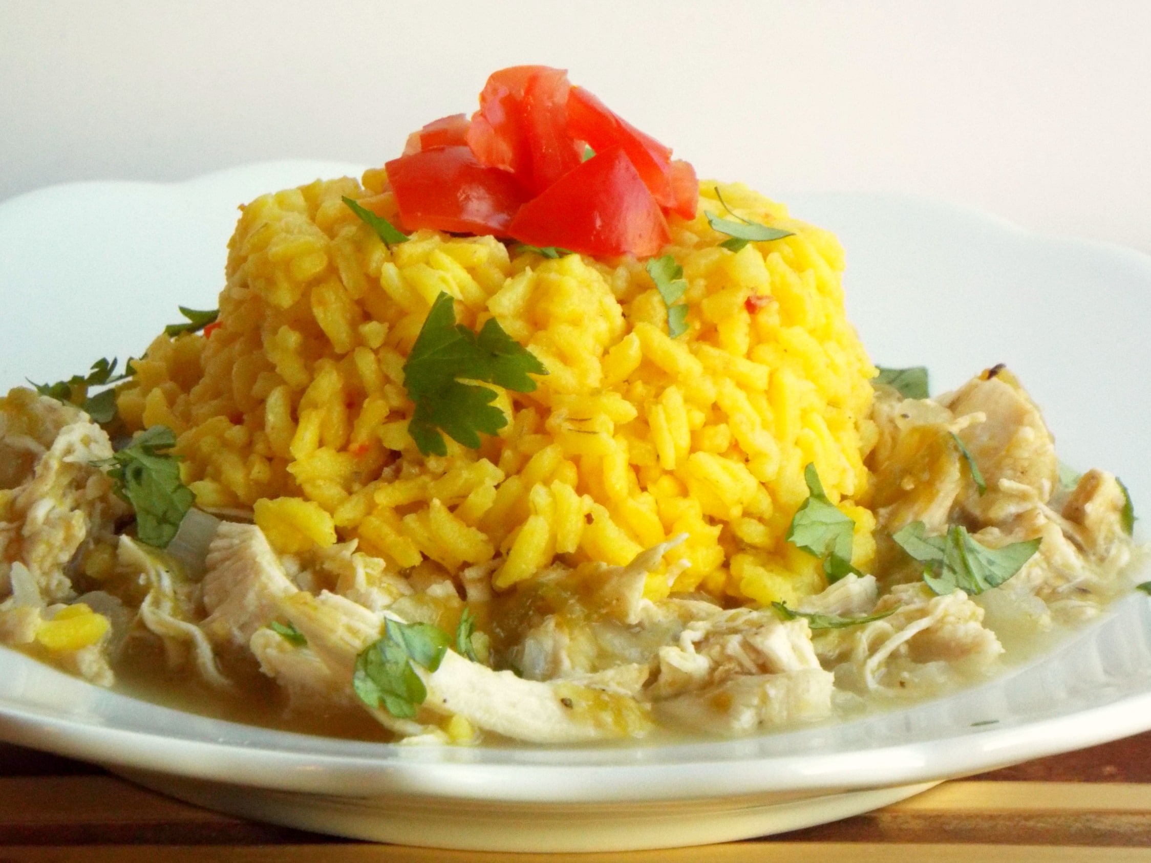 A plate of shredded chicken topped with yellow rice, tomatoes and cilantro