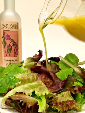 Champagne Vinaigrette dressing being poured on a lettuce salad with bottle in background