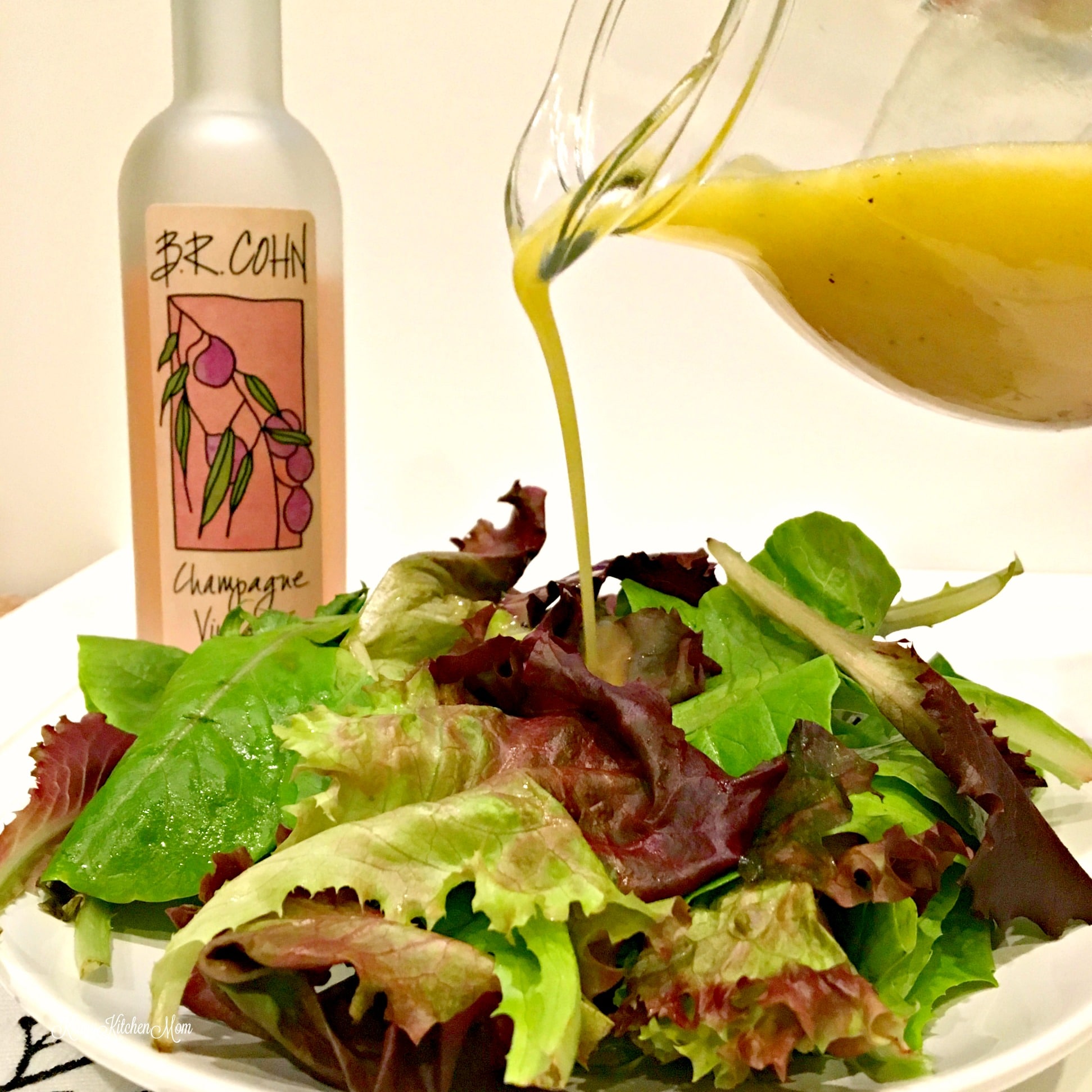 Champagne Vinaigrette dressing being poured on a lettuce salad with bottle in background