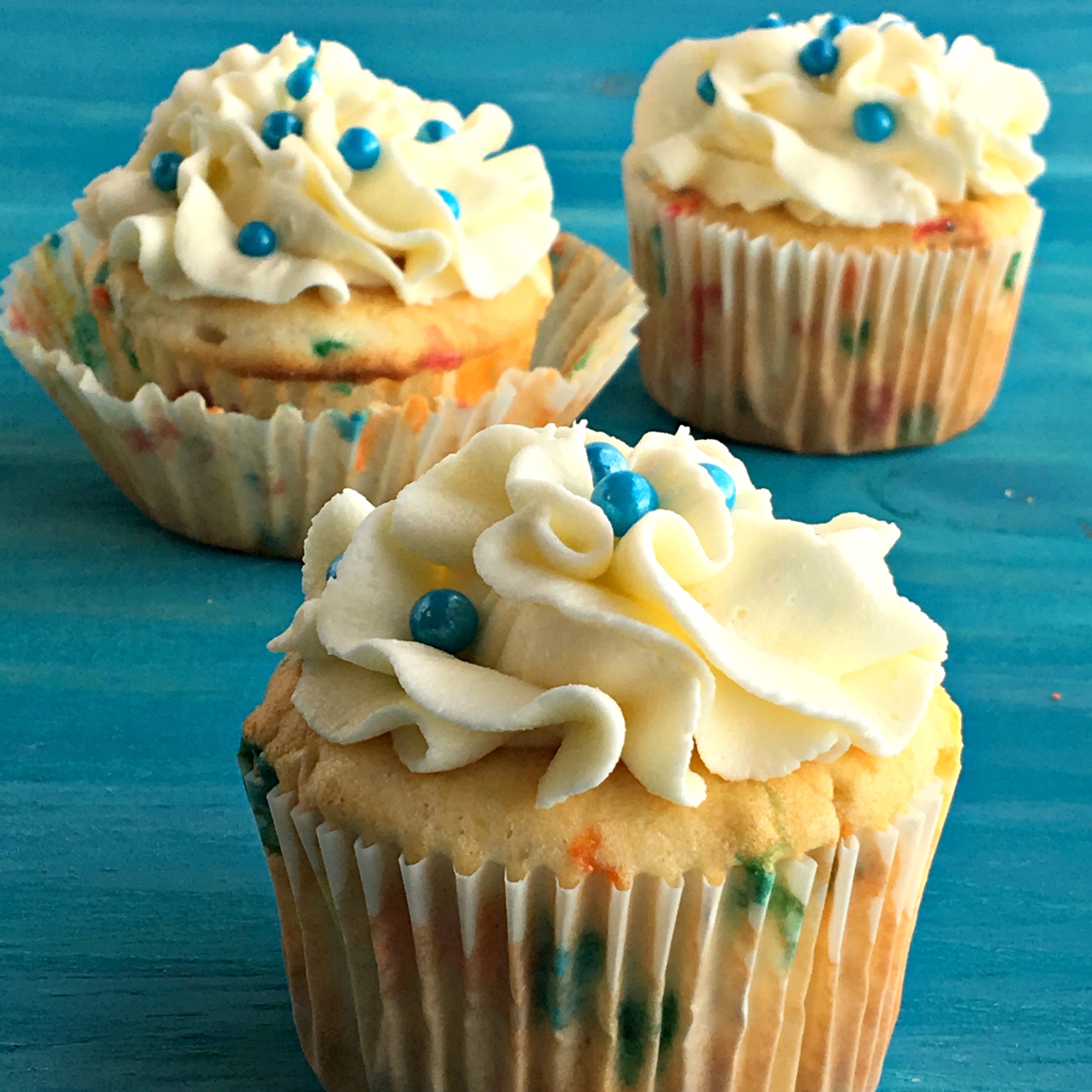 three cupcakes with blue sprinkles on a blue board