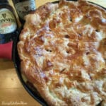 A pie in a skilled with beer bottle in background