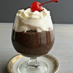 a fancy dish of chocolate pudding topped with whipped cream and a cherry