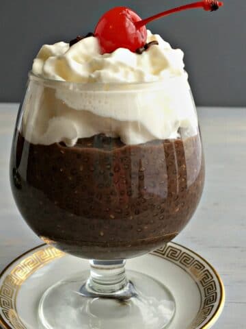 a fancy dessert dish with chocolate pudding topped with whipped cream and cherry