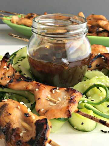 chicken kabobs and cucumber slices with a jar of sauce