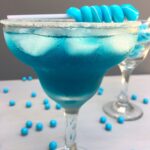 a close up of a blue cocktail with a blue candy stick sitting on top