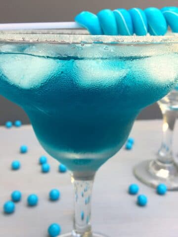 a close up of a blue cocktail with a blue candy stick sitting on top