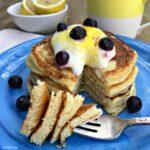 a stack of pancakes with whipped cream and blueberries on top and a fork on a blue plate