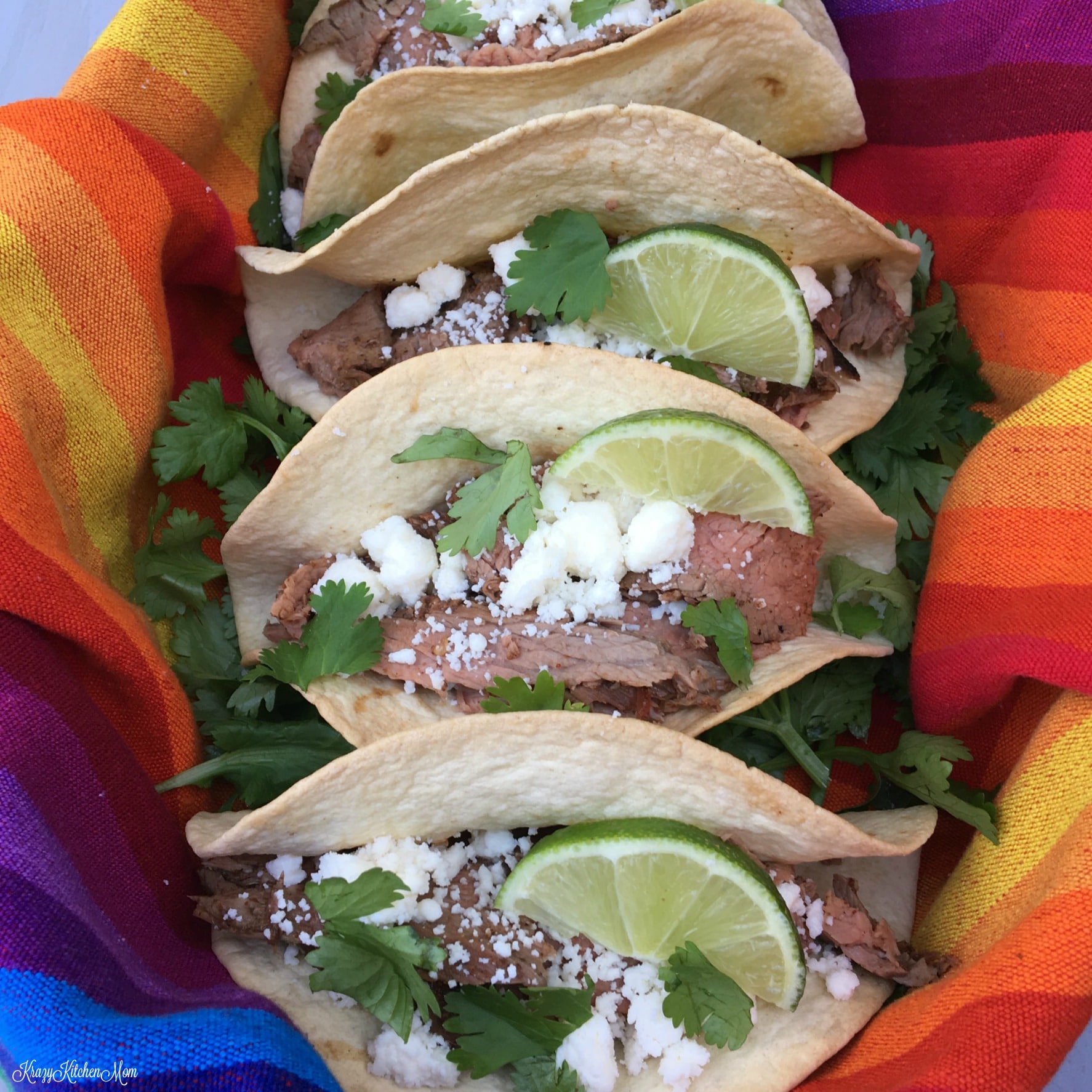 a row of four tacos topped with cheese, lime and cilantro