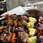 Pork, pepper, pineapple skewers with bowl of sauce and brush in background