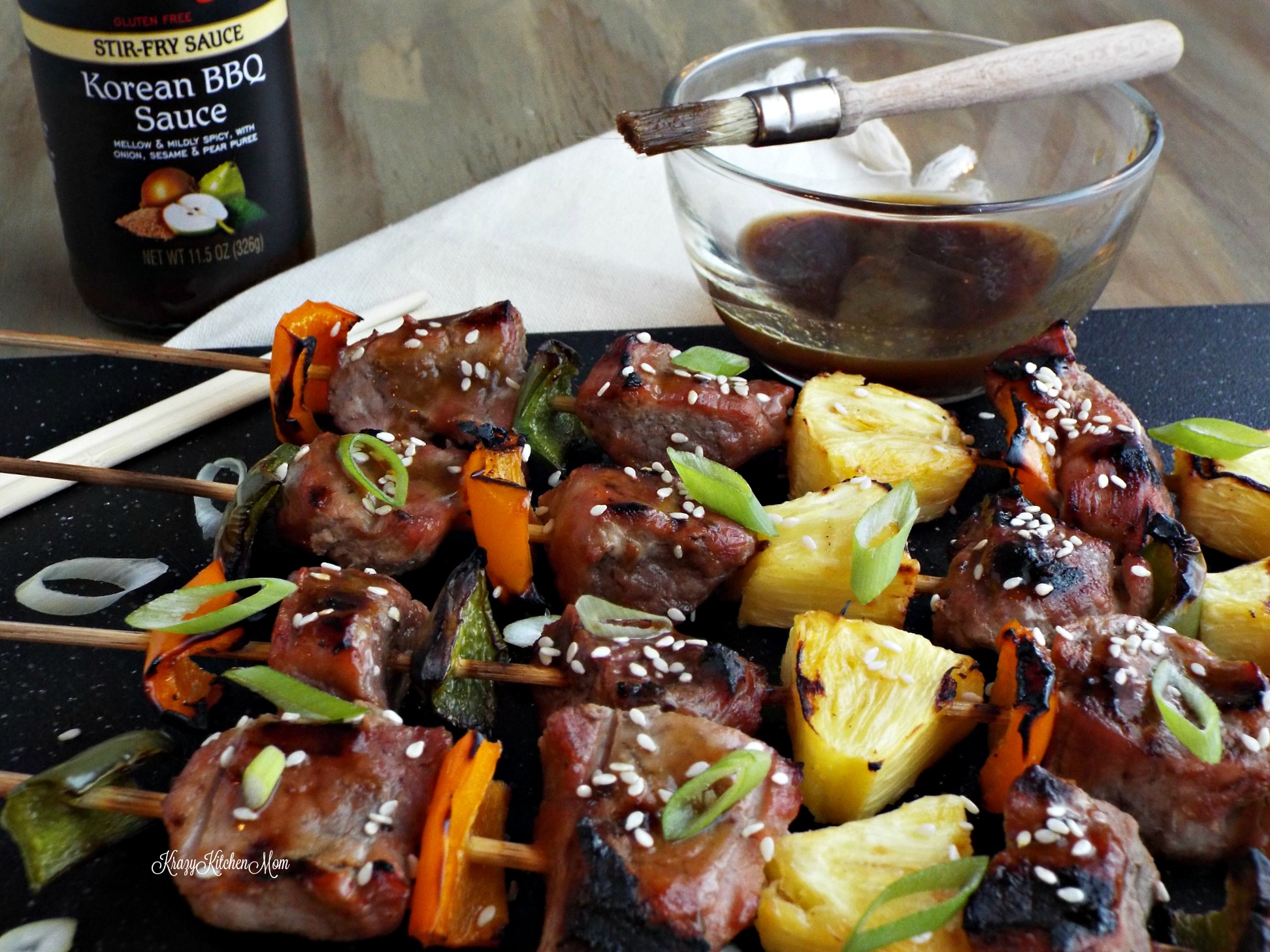 Pork, pepper, pineapple skewers with bowl of sauce and brush in background