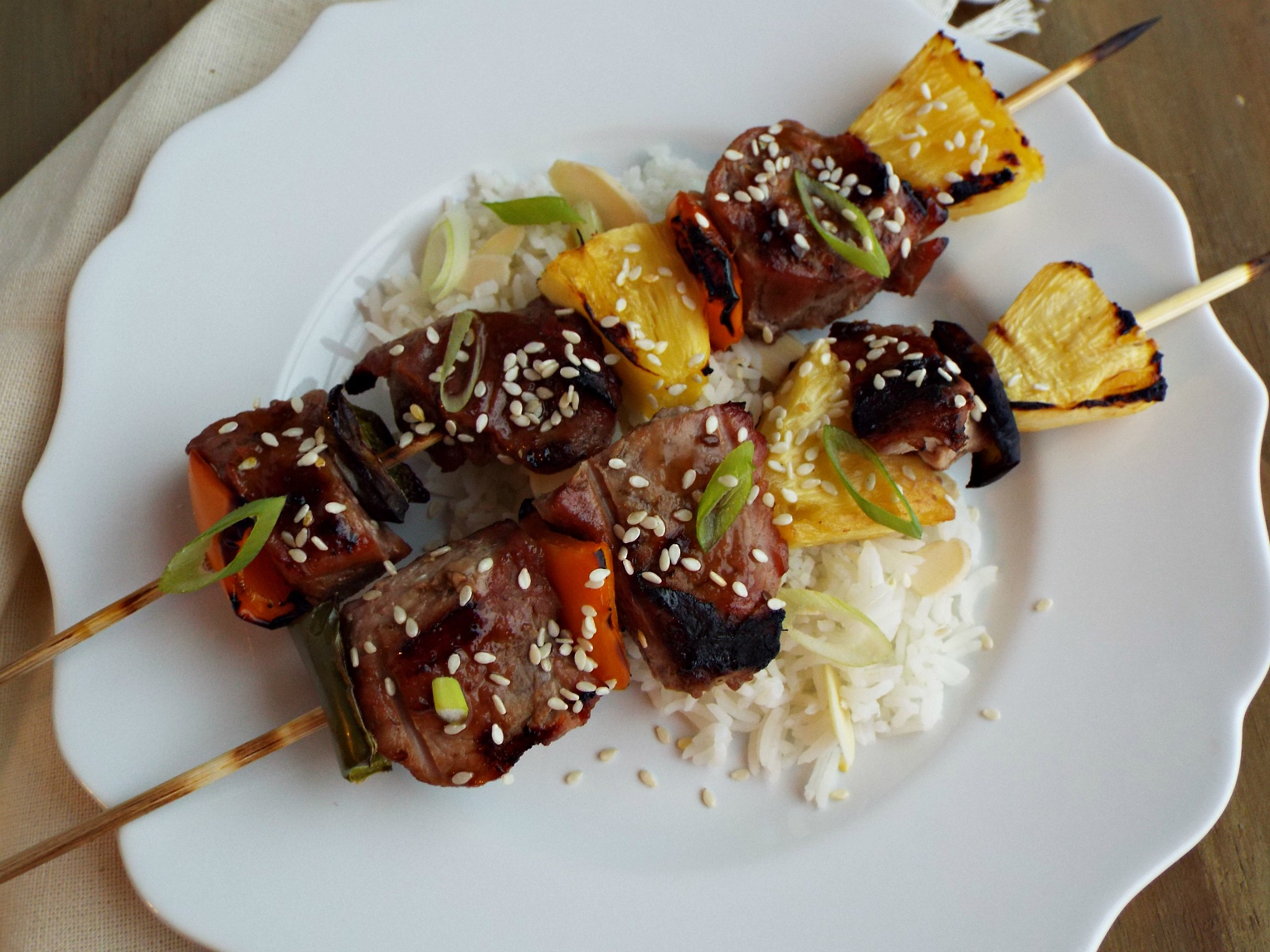 two pork, pepper, pineapple kabobs sitting on white rice