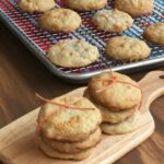 two stacks of three cookies wrapped with string on a small cutting board with cookies on rack in background