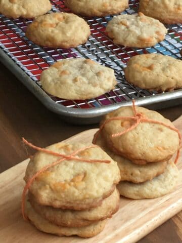 two stacks of three cookies wrapped with string on a small cutting board with cookies on rack in background