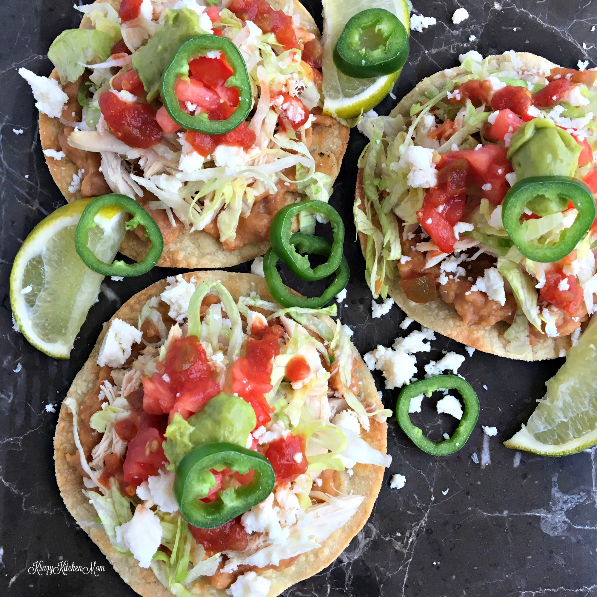 three flat tortillas topped with beans, tomatoes, chicken, jalapeños, and guacamole