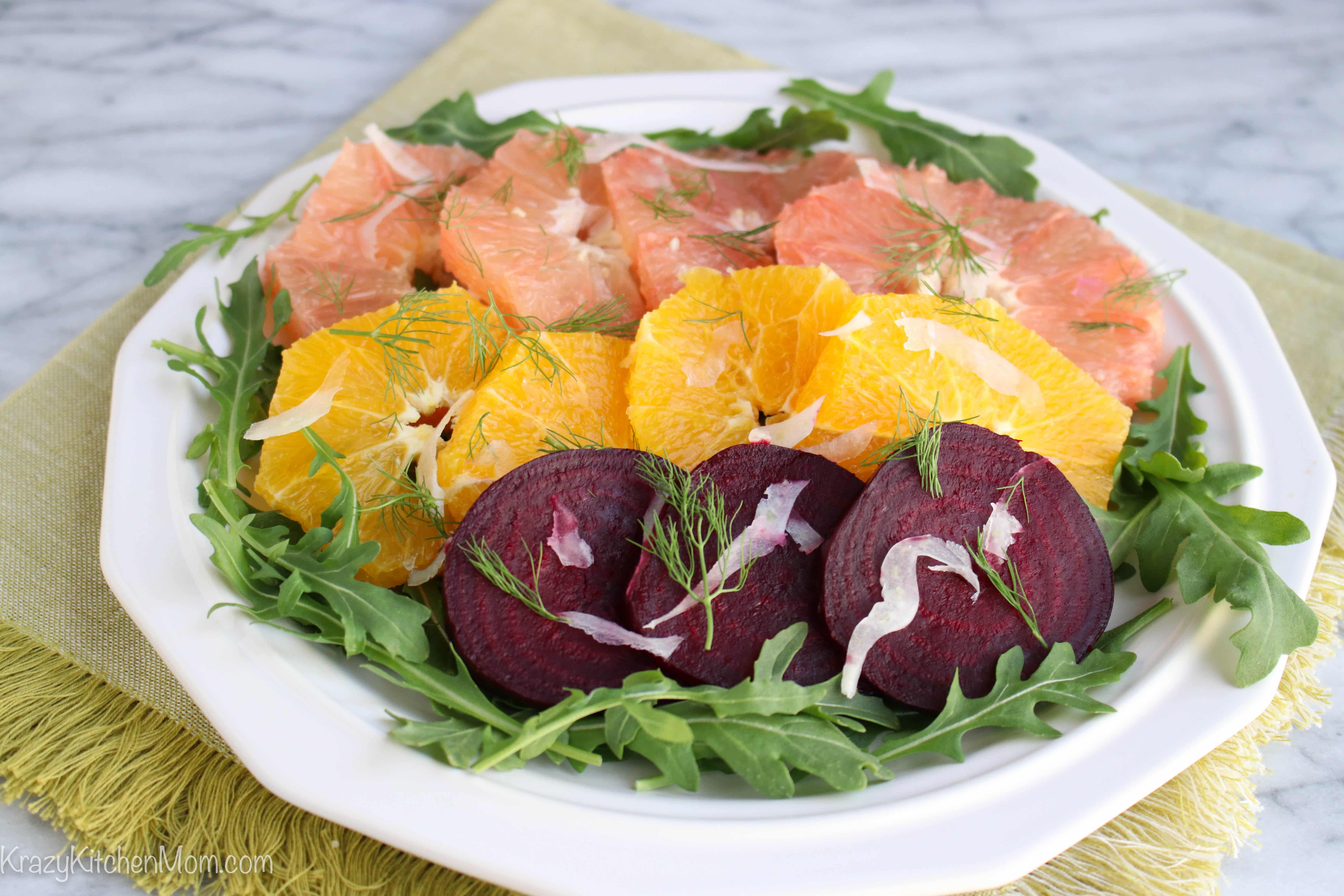 a white plate with grapefruit, orange and beet slices with arugula
