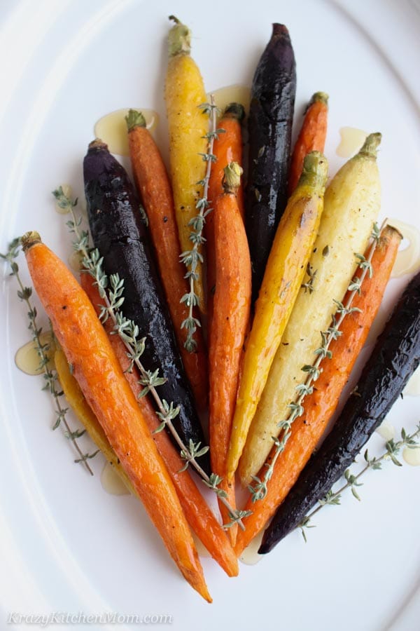 Orange, yellow, purple carrots with fresh thyme and honey on a white plate