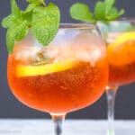 Close up shot of an glass filled with aperol spritz garnished with lemon slice and fresh mint