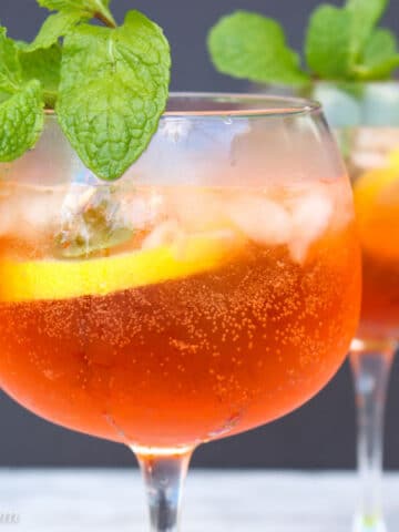 Close up shot of an glass filled with aperol spritz garnished with lemon slice and fresh mint