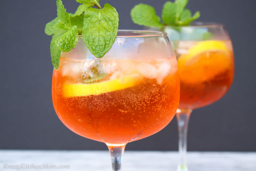 Close up shot of an glass filled with aperol spritz garnished with lemon slice and fresh mint