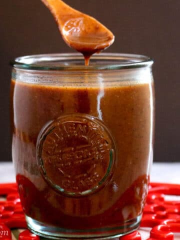 Jar of Enchilada and Sauce with a small wooden spoon dipping into the sauce