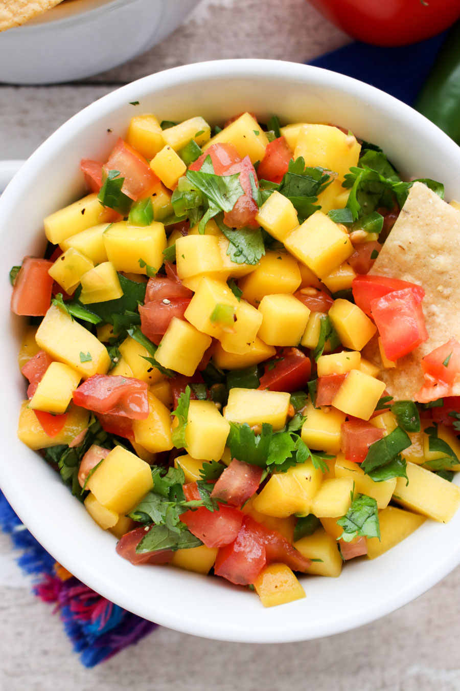 Mango salsa in a white bowl with a one chip in the salsa.