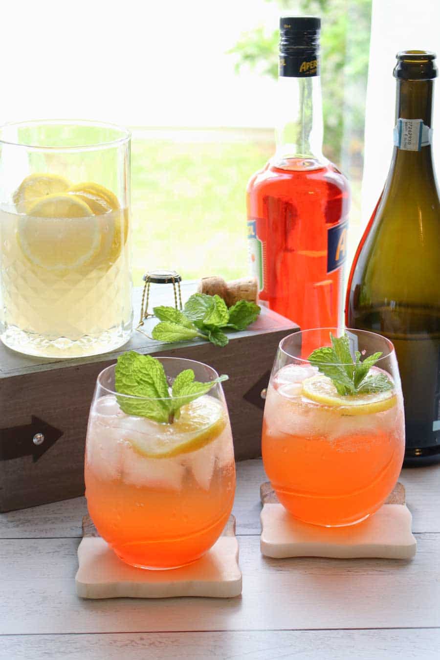 two cocktail garnished with lemon and mint with bottles in background
