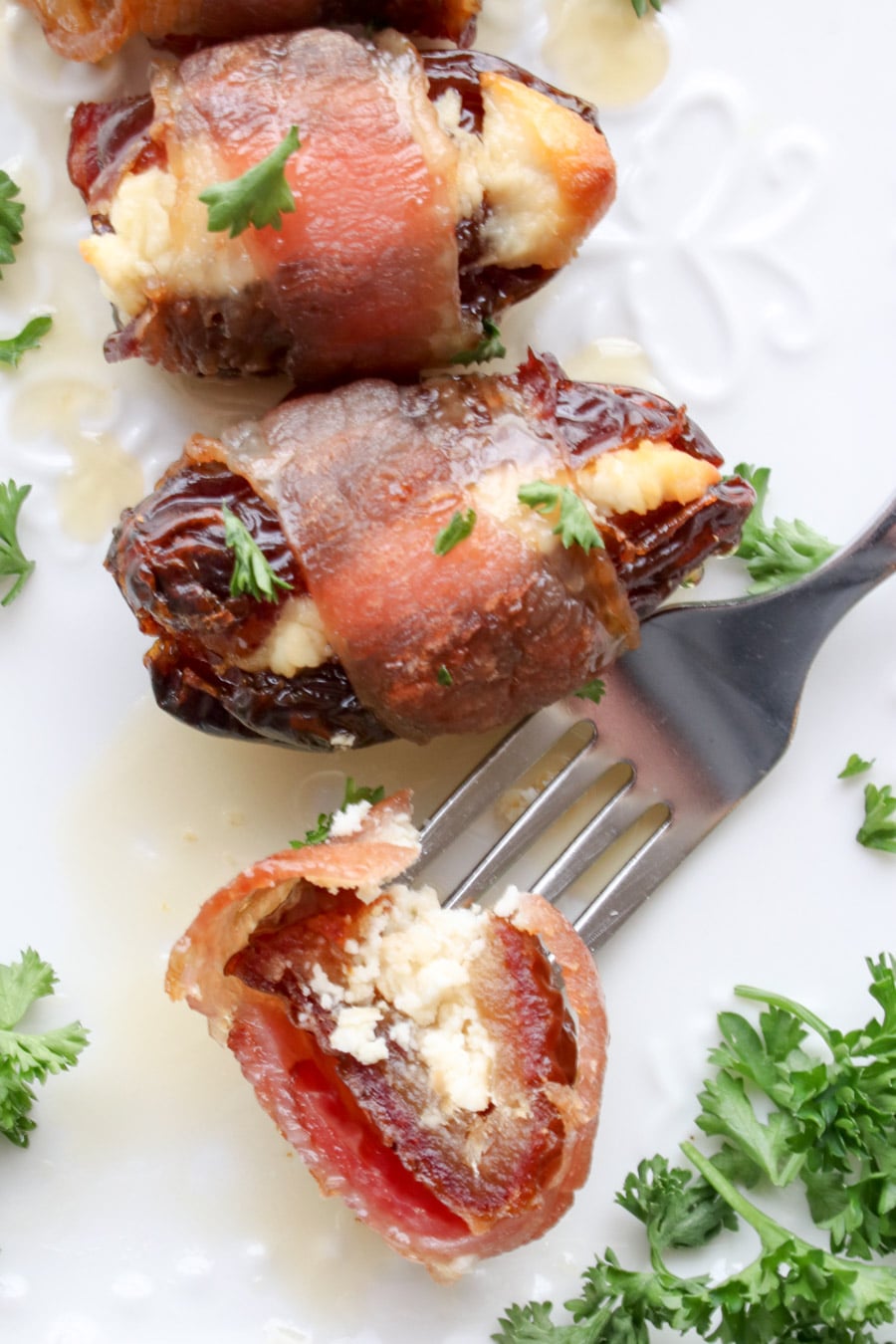 A close up of a plate of bacon wrapped stuffed date on a fork