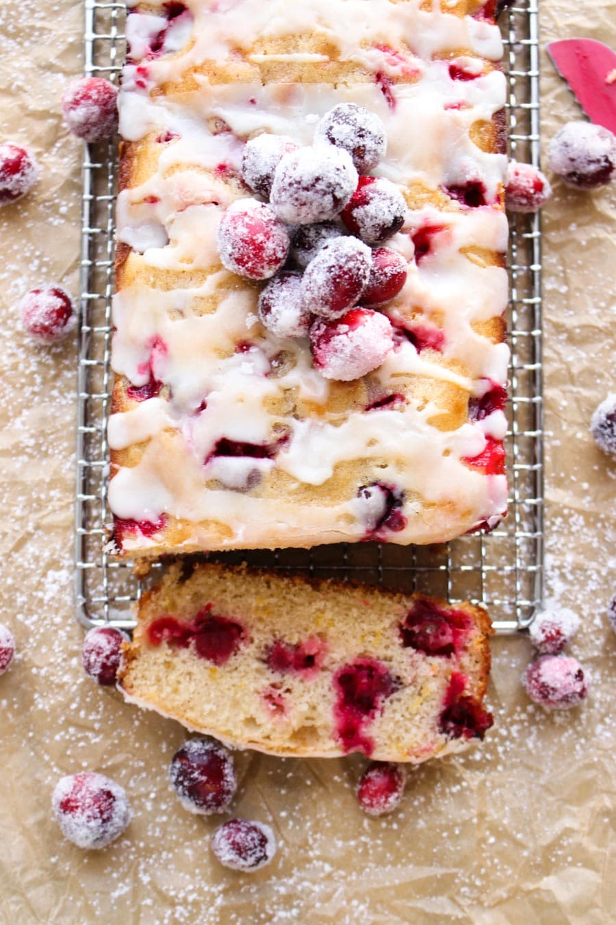 A close up of a piece of cranberry coffee cake topped with white glaze and cranberries sitting on a serving rack