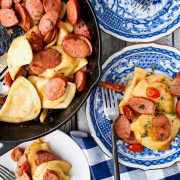skillet of sausage and pierogis with blue plates on side. One plate is empty